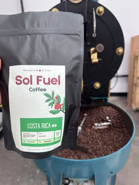 coffee bag labeled 'Sol Fuel Coffee' held above a coffee roaster filled with beans.