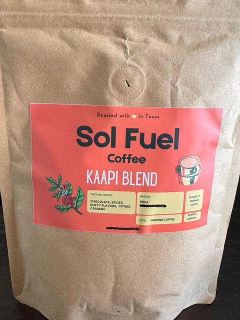 A stand-up kraft paper coffee bag labeled Sol Fuel Coffee Kaapi Blend, photographed on a dark tabletop with a blurred indoor background.